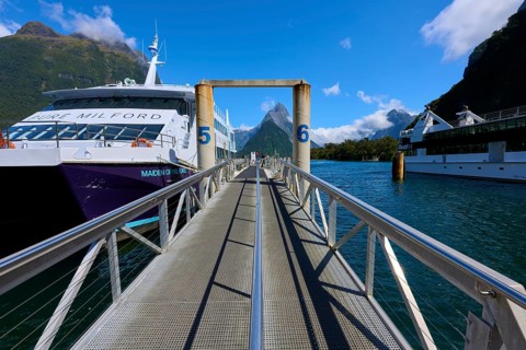 Metal walkway leads between large ships to a picturesque mountain and fjord backdrop, summer,