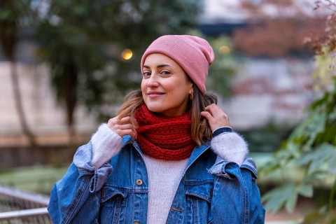 Happy woman wearing stylish winter clothes, playfully adjusting her red scarf while enjoying a