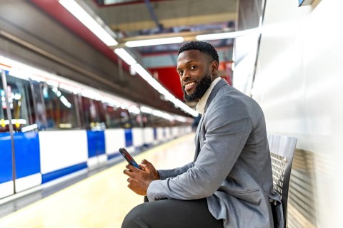 Young businessman is sitting on bench in subway station and using smartphone while waiting for