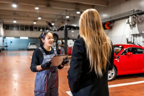 Smiling female mechanic explaining repair details to a customer while delivering a car in a modern