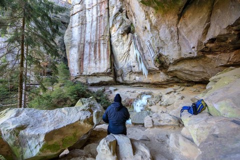 Hiker taking a break, frozen waterfall with icicles in the Gautschgrotte, Hohnstein, Saxony,