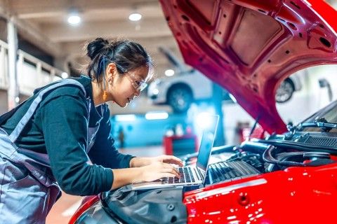 Young female mechanic using a laptop while performing diagnostics on a red car in a modern auto