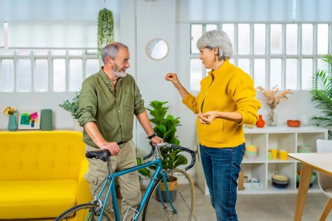 Senior couple talking while holding bike in the apartment. Sustainable way of life