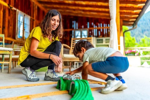 Mom and child enjoying playtime together, building a car track on the porch of their cozy wooden