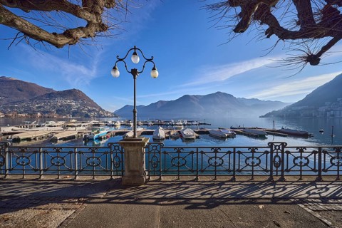 Lantern, forged railing, lakeside promenade, shadow, marina, trees, motorboats, hill with village,