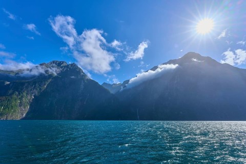 Bright sun over majestic mountains and calm sea, summer, Milford Sound, Te Anau, Fiordland National
