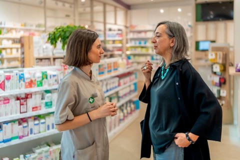 Side view of a female young pharmacist and woman standing in the store talking