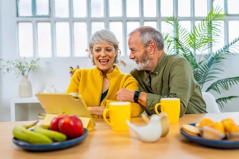 Happy senior couple using digital tablet at home while eating healthy breakfast