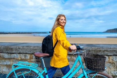 Tourist walking with her bicycle along the beach wall on a cloudy day, enjoying the fresh air and