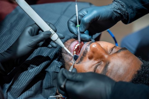 Close up of a dentist using specialized tools during a teeth whitening session on a male patient,