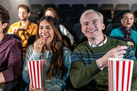 Young couple enjoying a movie at the cinema, eating popcorn and smiling, surrounded by other people