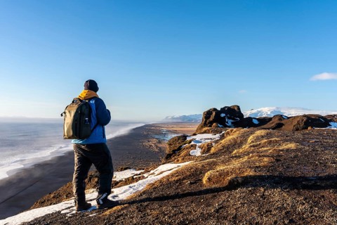 A tourist man with his back turned at the viewpoint of Dyrholaey beach in the cold winter with snow