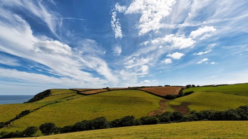Hilly landscape with fields, meadows, hedges by the sea, spring clouds in summer, Cirrus, Cornwall,