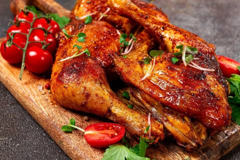 Grilled fried chicken legs, served with fresh cherry tomatoes, and herbs, on a wooden chopping