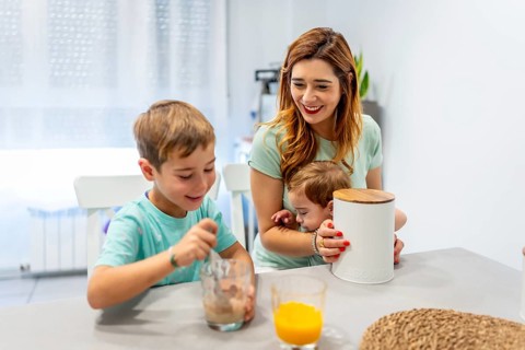 Mother holding a baby and having breakfast with her son at home in the morning