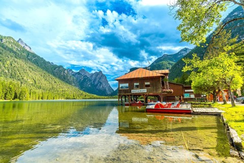Stunning view of lake dobbiaco with pedal boats and a restaurant, surrounded by the majestic peaks