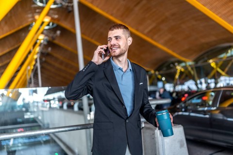 Businessman holding a reusable water bottle and a suitcase while talking on his smartphone at the