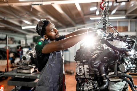 Skilled mechanic working diligently on a car engine while utilizing a crane in a modern auto repair
