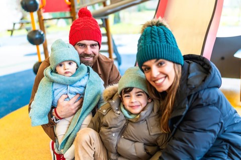Smiling family wearing winter clothes and woolen hats, spending time together at the playground