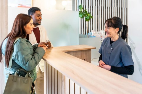 Interracial couple filling out paperwork at the reception desk of a modern dental clinic,