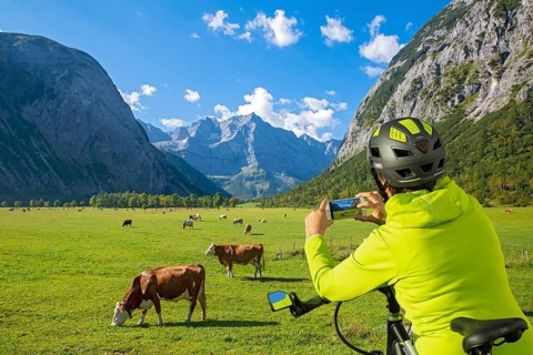 A biker uses her mobile phone to photograph the Großer Ahornboden and the grazing cows, Großer