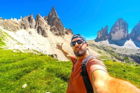 Hiker taking a selfie with the tre cime di lavaredo in the background, during a summer hike in the