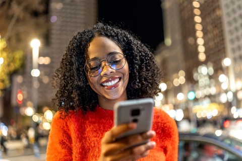 Smiling woman using her smartphone while enjoying the vibrant urban nightlife, surrounded by