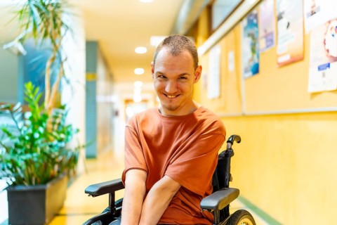 Man with disability sitting in wheelchair smiling at camera in the corridor of coworking