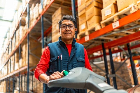 Low angle view portrait of a cheerful latin warehouse worker using machinery