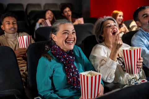 People of different ages laughing and eating popcorn while watching a movie in the cinema
