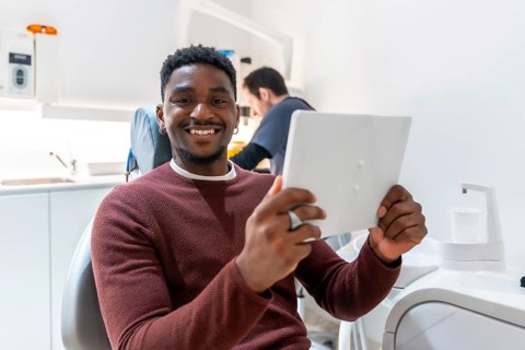 Smiling patient using digital tablet, possibly reviewing treatment plan or x rays, while dentist