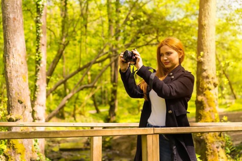 Woman photographer with a black jacket enjoying in an autumn park, taking pictures at sunset on a