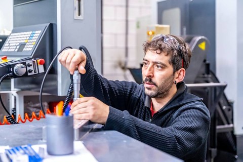 Concentrated engineer crouching fixing a piece of metal in a cnc modern factory