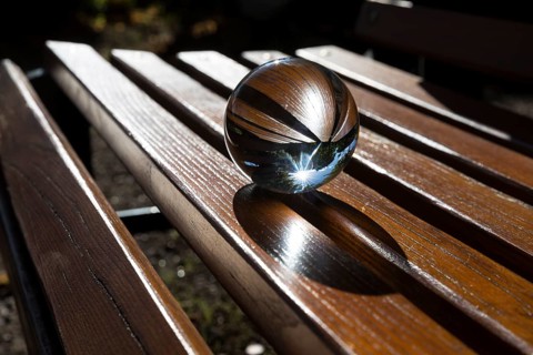 Glass ball lying on a bench with wooden slats, reflecting the sun, Saxony, Germany, Europe