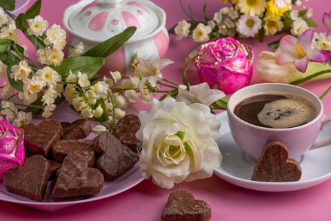 Coffee mug with heart-shaped chocolate and flowers on a pink background, Valentine's Day