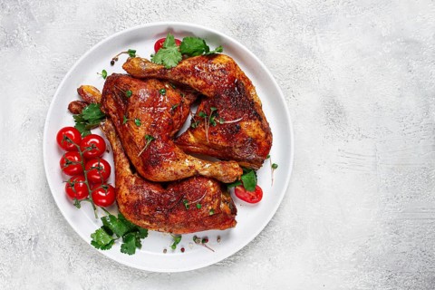 Grilled fried chicken legs, served, with fresh cherry tomatoes, and herbs, on a white plate,