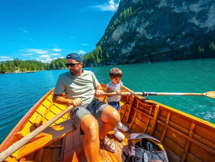 Father and son enjoying a summer day rowing a wooden boat on lake braies with the stunning