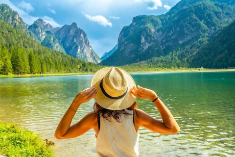 Young woman holding her straw hat admiring the landscape of lake dobbiaco and the dolomites during