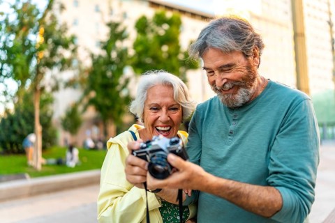 Happy senior couple looking at the photos in a camera standing in the city street