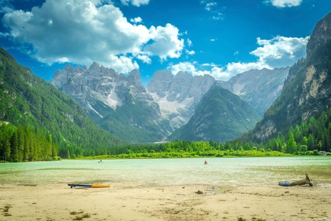 Tourists swimming and paddleboarding in the turquoise waters of lago di landro, surrounded by the