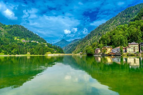 Tranquil summer scene at lake alleghe with colorful houses reflected in the emerald water,