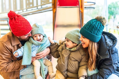 Cheerful family bundled in warm winter clothes, enjoying playful moments together on a playground