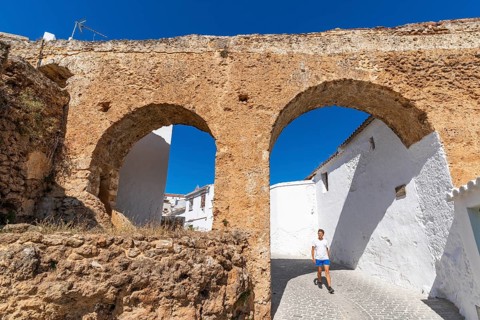A man walks through an arch under a historic aqueduct in the white village of Yunquera, Sierra de