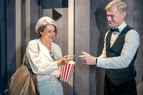 Elegant mature woman handing ticket to smiling usher while holding popcorn bucket, ready to enjoy