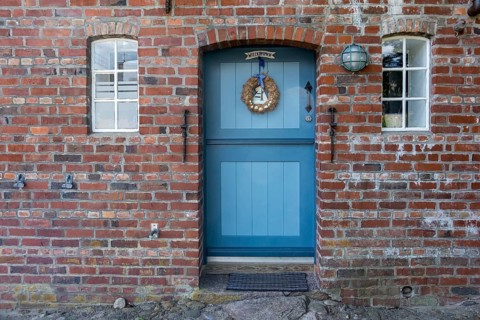 Blue wooden door in red brick wall with two windows and decorations, Föhr, Nordfriesland,
