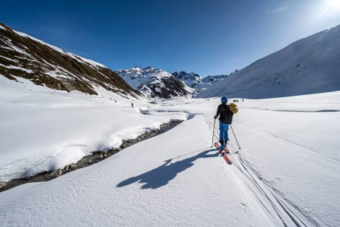 Ski tourer in the snow by a mountain stream in the Funtauna Valley, Graubünden Haute Route, Albula
