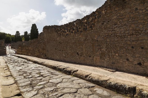 Long narrow stone sidewalk and street made of large grey smooth and worn lava stones plus remnant