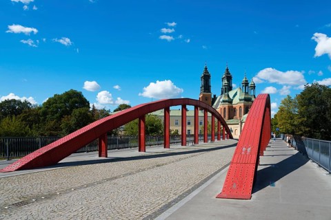 A modern red bridge leads to the cathedral in the background with blue sky and white clouds,