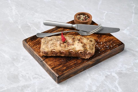 Roasted pork ribs on a rustic wooden board, accompanied by a knife and fork. A small bowl of mixed