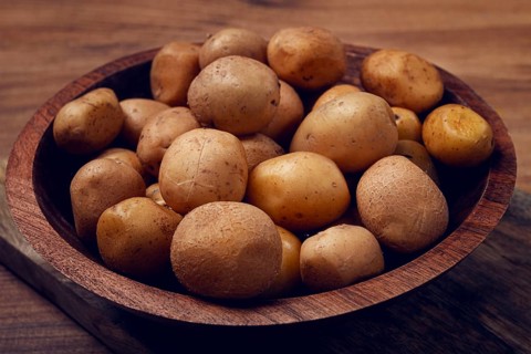 A wooden bowl filled with freshly harvested small potatoes sits on a rustic wooden surface,